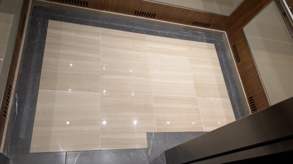 Marble elevator lobby floor in an Olympic Village building after polishing, the entrance doors reflected in the stone