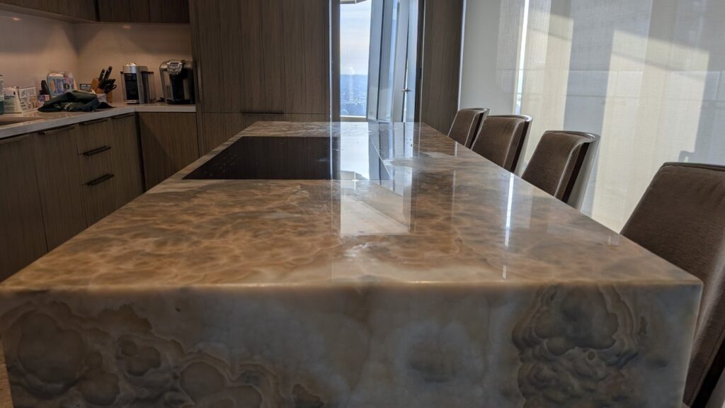 Figured amber onyx kitchen island with chairs along it, the top matte and dull, before polishing