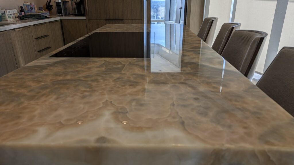 Figured amber onyx kitchen island in a downtown Vancouver condo after polishing, the window reflected in the top
