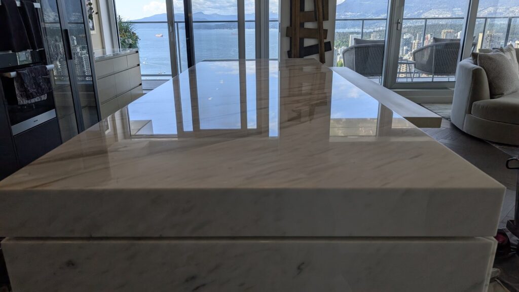 White marble kitchen island in a downtown Vancouver home after restoration, polished, with the water visible through the windows behind