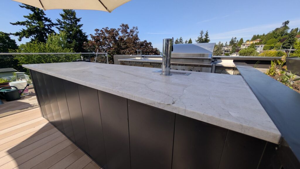 Quartzite island in an outdoor kitchen on a White Rock deck after restoration, under a blue sky