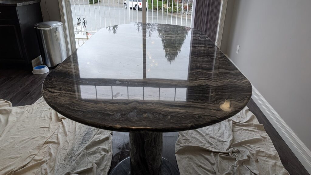 The same dark marble table after honing and polishing, with the window frames reflected in a mirror finish