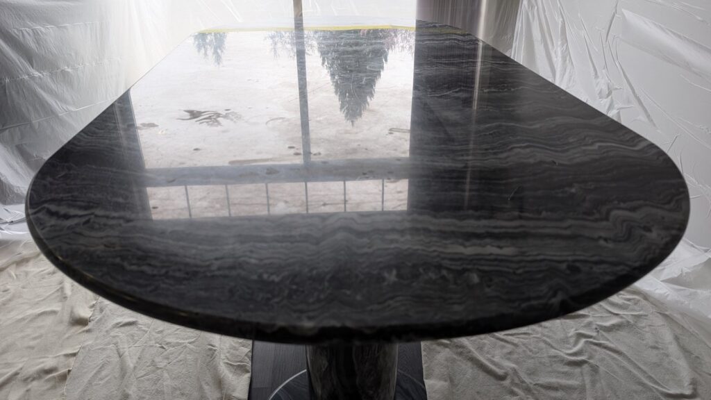 Dark grey marble dining table with pale hazy patches of etching across the top, before restoration