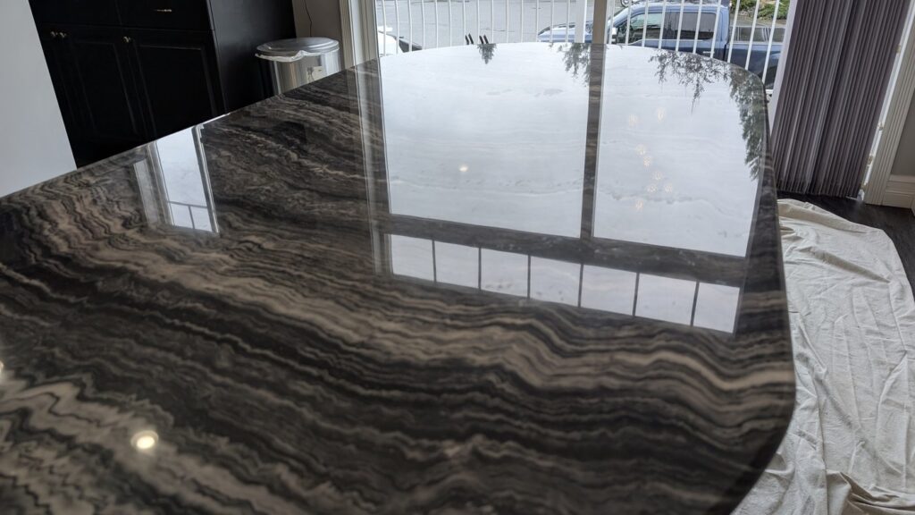 Close view of the same dark marble table top after polishing, the etch marks gone and the veining sharp