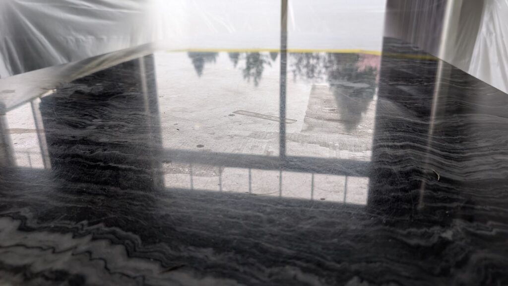 Close view of grey etch marks on a dark marble table top, before restoration