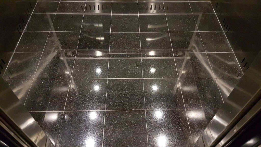 The same black granite elevator floor after polishing, the ceiling lights reflected in the stone