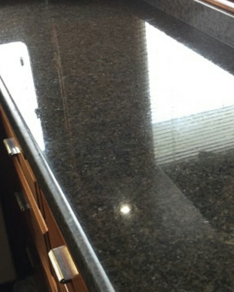 The same dark granite counter after polishing, the window blinds reflected in the surface