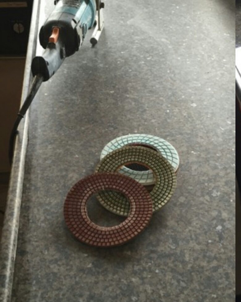 Dark granite kitchen counter, dull, with the polisher and polishing pads set out on it before work