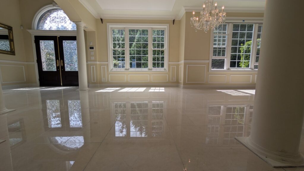 Cream marble hall floor with an inlaid border in a West Vancouver home after polishing, the doors reflected in the stone