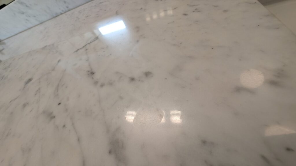 Close view of a white marble vanity top with hazy dull etch marks across the polished surface
