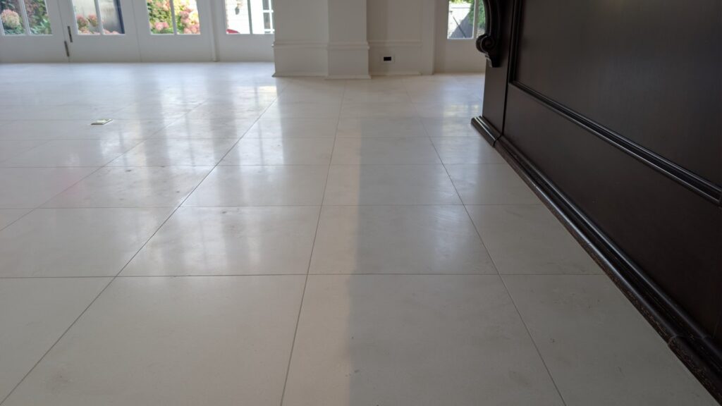 The same limestone floor beside the dark wood cabinetry after restoration, the tiles clean and even with window light reflected softly