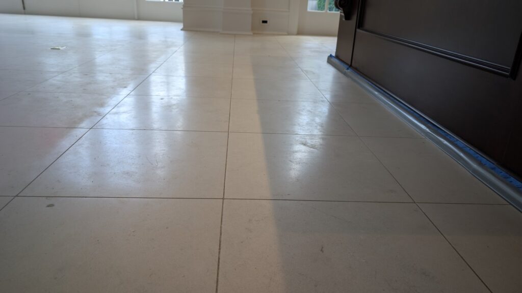 Pale limestone floor tiles beside dark wood cabinetry in a Point Grey home, greyer and scuffed, with painter's tape along the cabinet base, before restoration