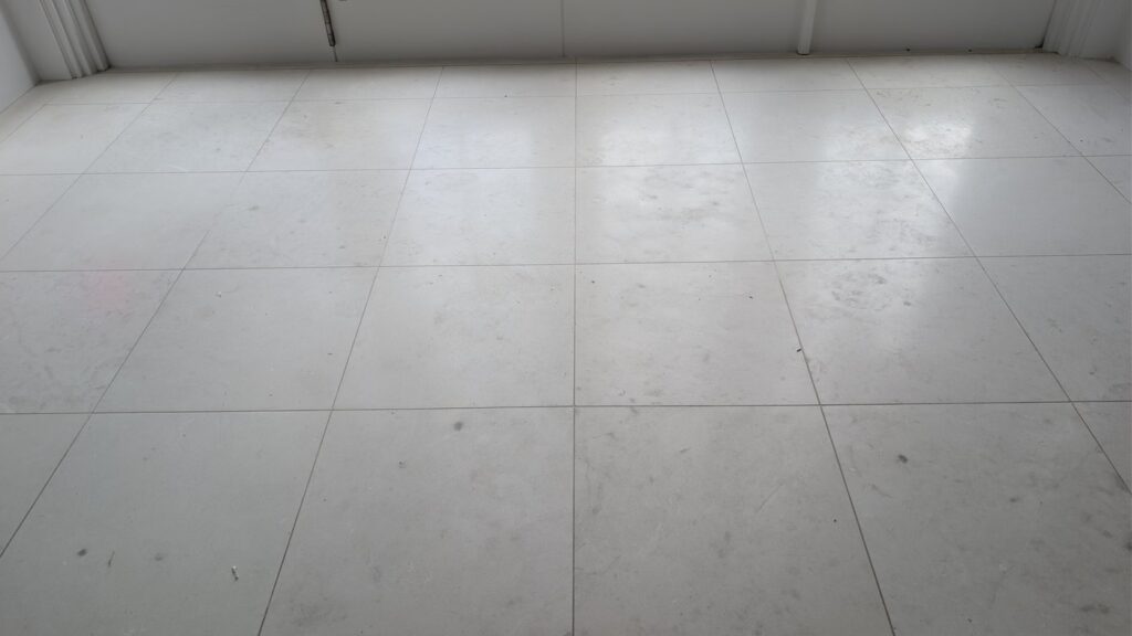 Large pale limestone tiles across an open room in a Point Grey home, grey and spotted with scuffs, before restoration