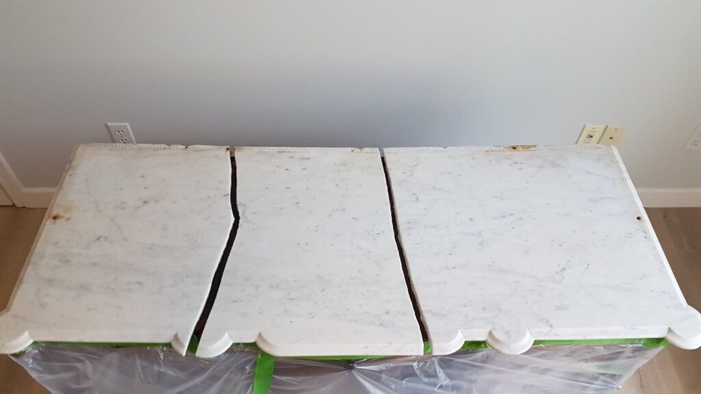 White marble top of an antique cabinet broken into three pieces, laid out on plastic before repair