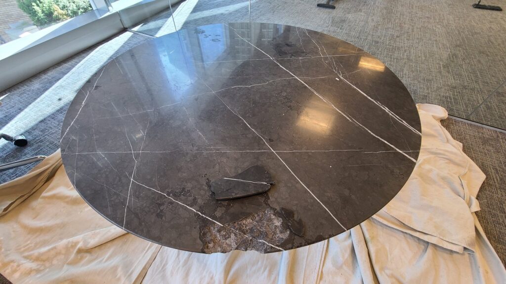 Round dark marble table with a large chunk missing from the edge, before repair