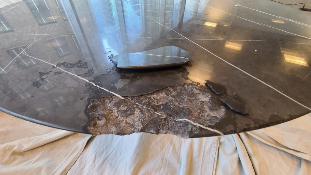 Close view of a round marble table edge with a large chunk broken away, before repair