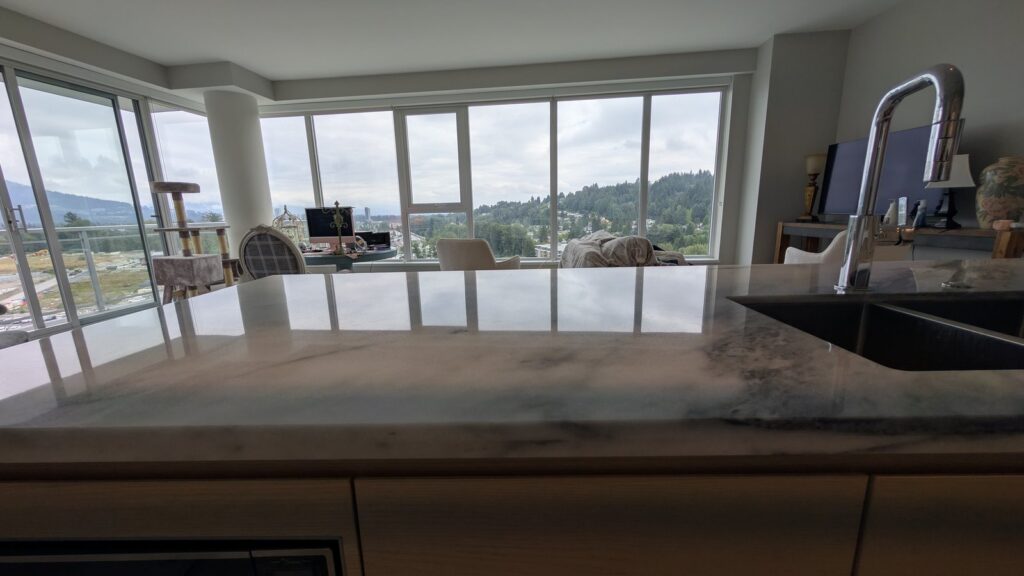Marble kitchen island in a Port Moody home after restoration, the polished top reflecting the windows and the view