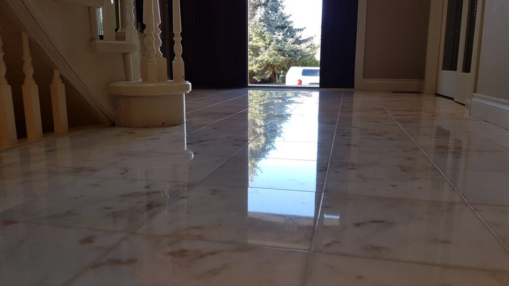The same cream marble entry hall floor after polishing, the front door and the trees outside reflected in it