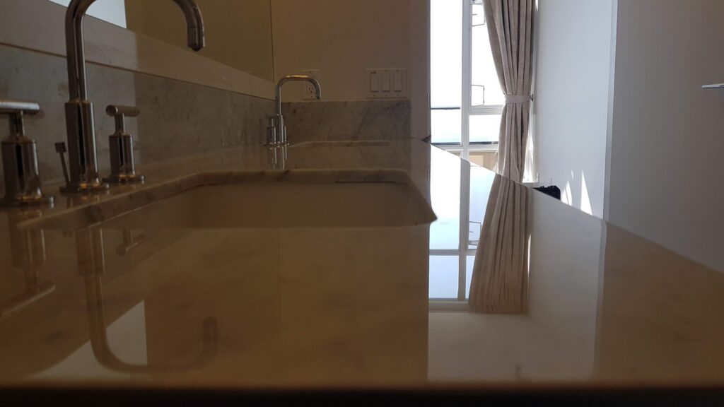 The same cream marble vanity top after polishing, the taps reflected in the surface