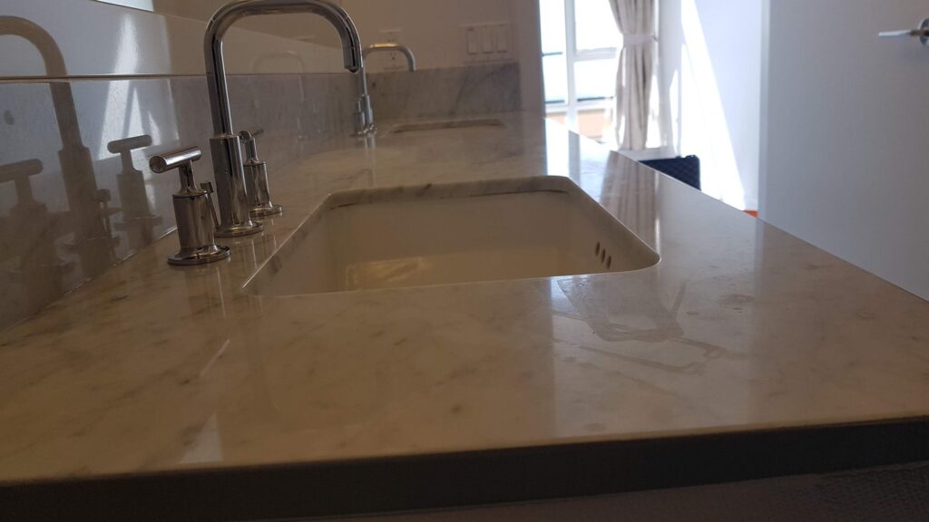 Cream marble bathroom vanity top around the basin, dull and water-marked, before restoration