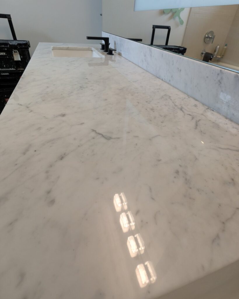 The same white marble vanity top after polishing, the lights reflected crisply along its length
