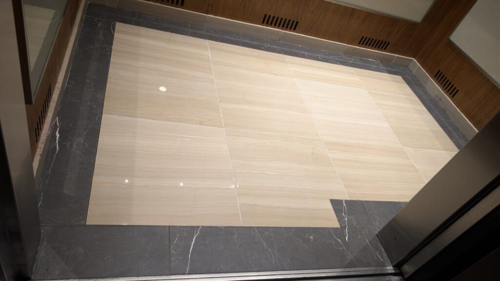 The same Olympic Village elevator lobby floor after polishing, the doors and planters reflected in the marble