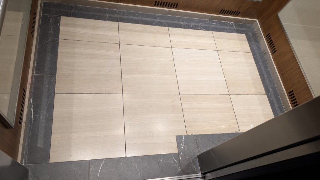 Marble elevator lobby floor in an Olympic Village building, dull and scuffed by traffic, before restoration