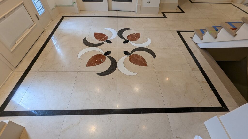 Cream marble entry floor with an inlaid medallion, flat and dull, before restoration
