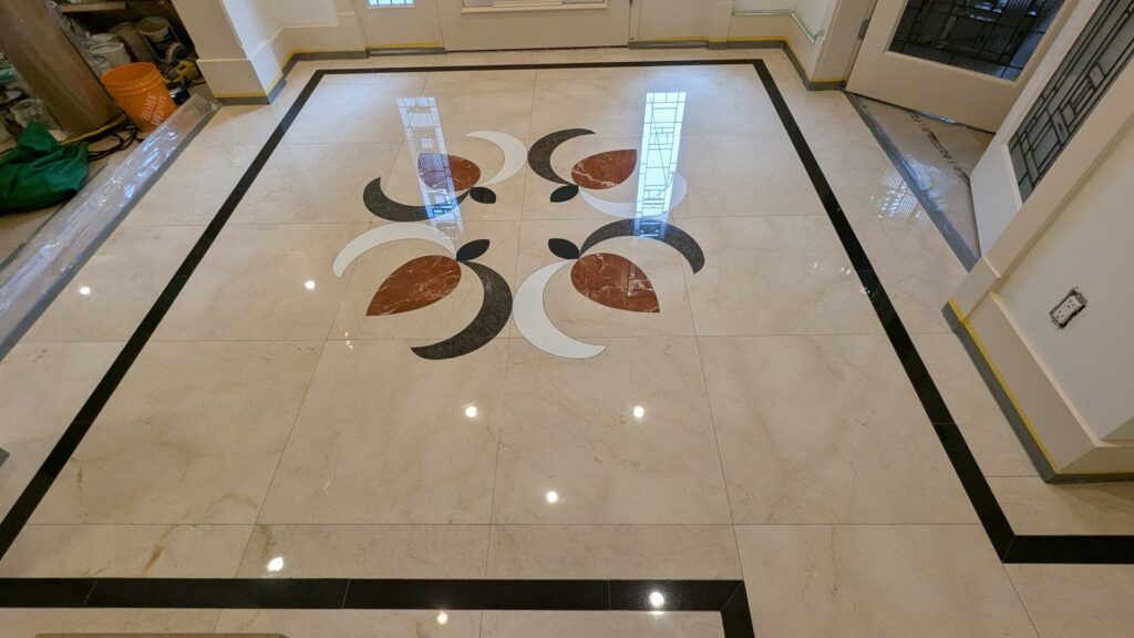 Cream marble entry floor in a Kitsilano home with a red, black and white inlaid medallion, polished and reflecting the doorway