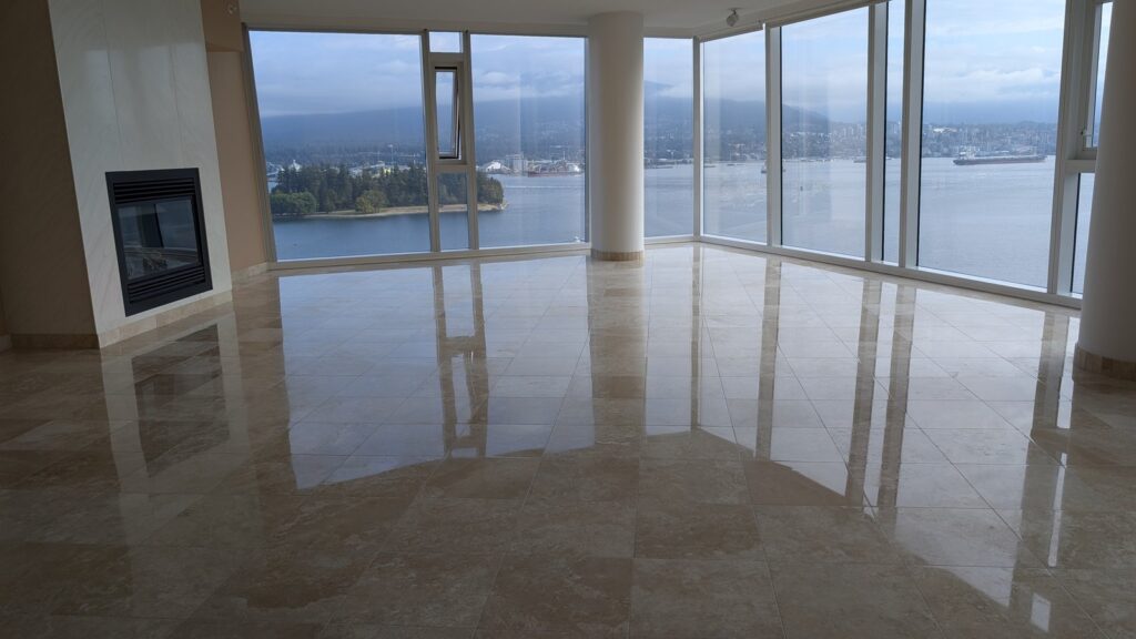 Travertine floor in a downtown Vancouver condo after restoration, polished and reflecting the harbour view through the windows