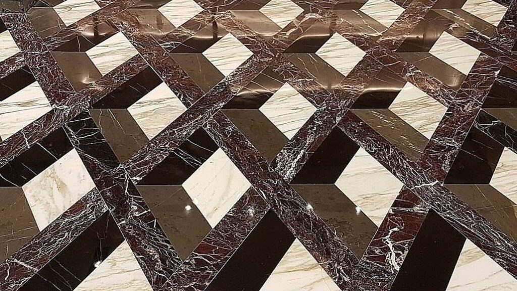 Polished marble mosaic floor in a tumbling-block pattern of cream, dark red and black stone, the lights reflected across it